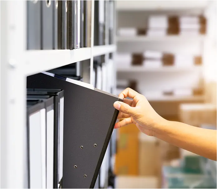 A hand pulling a black folder out of a rack of folders.